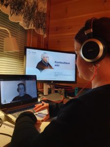 Nainen istuu kannettavan tietokoneen edessä kuulokkeet päässä.